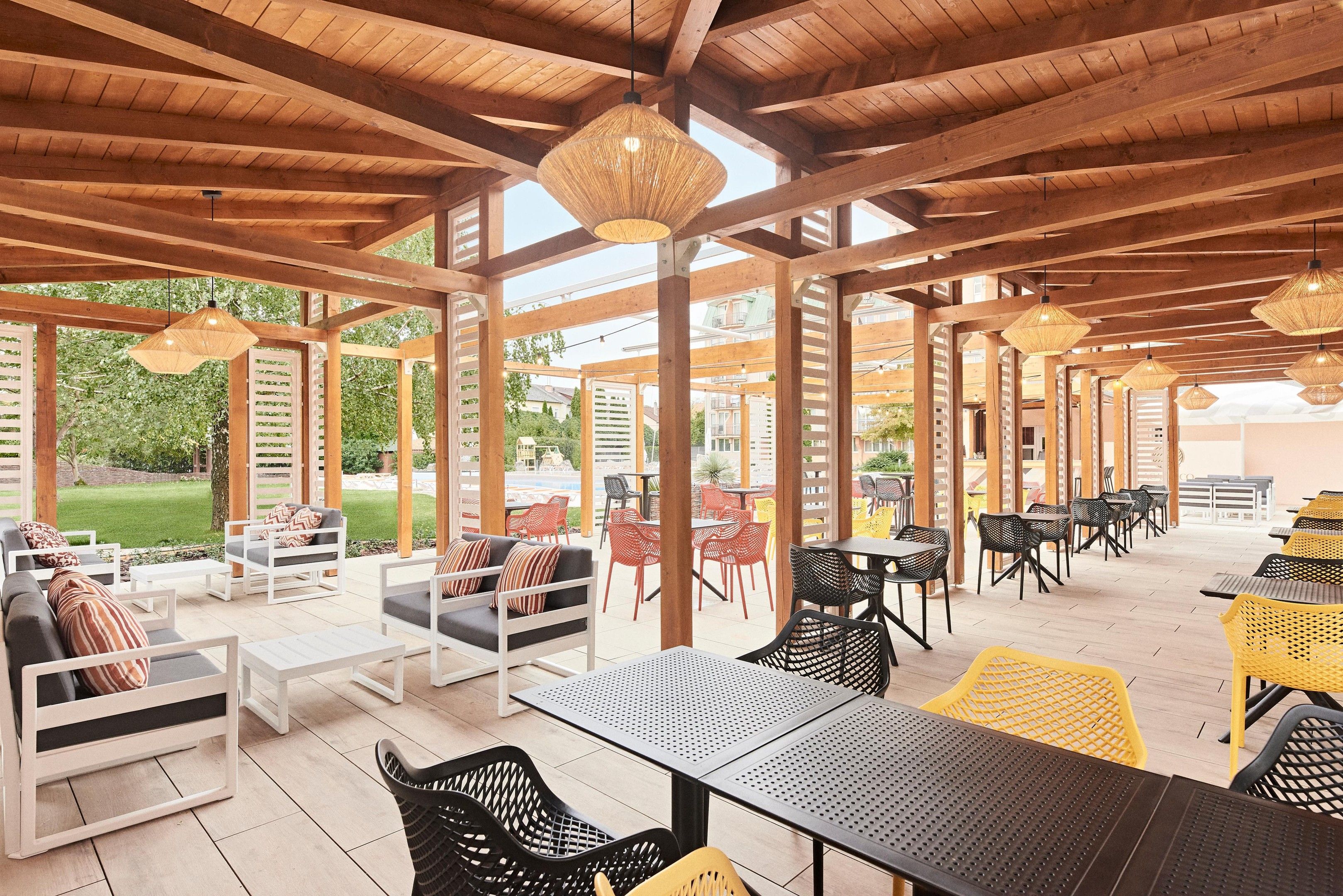 Un patio al aire libre con vigas de madera, mesas, sillas y luces colgantes.