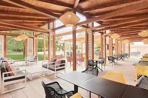 An outdoor patio with wooden beams, tables, chairs, and hanging lights. - Hotel Európa Fit (Hévíz)