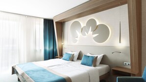 A hotel room with a large bed, two bedside tables, a chair, and a decorative wall panel. - Hotel Európa Fit (Hévíz)