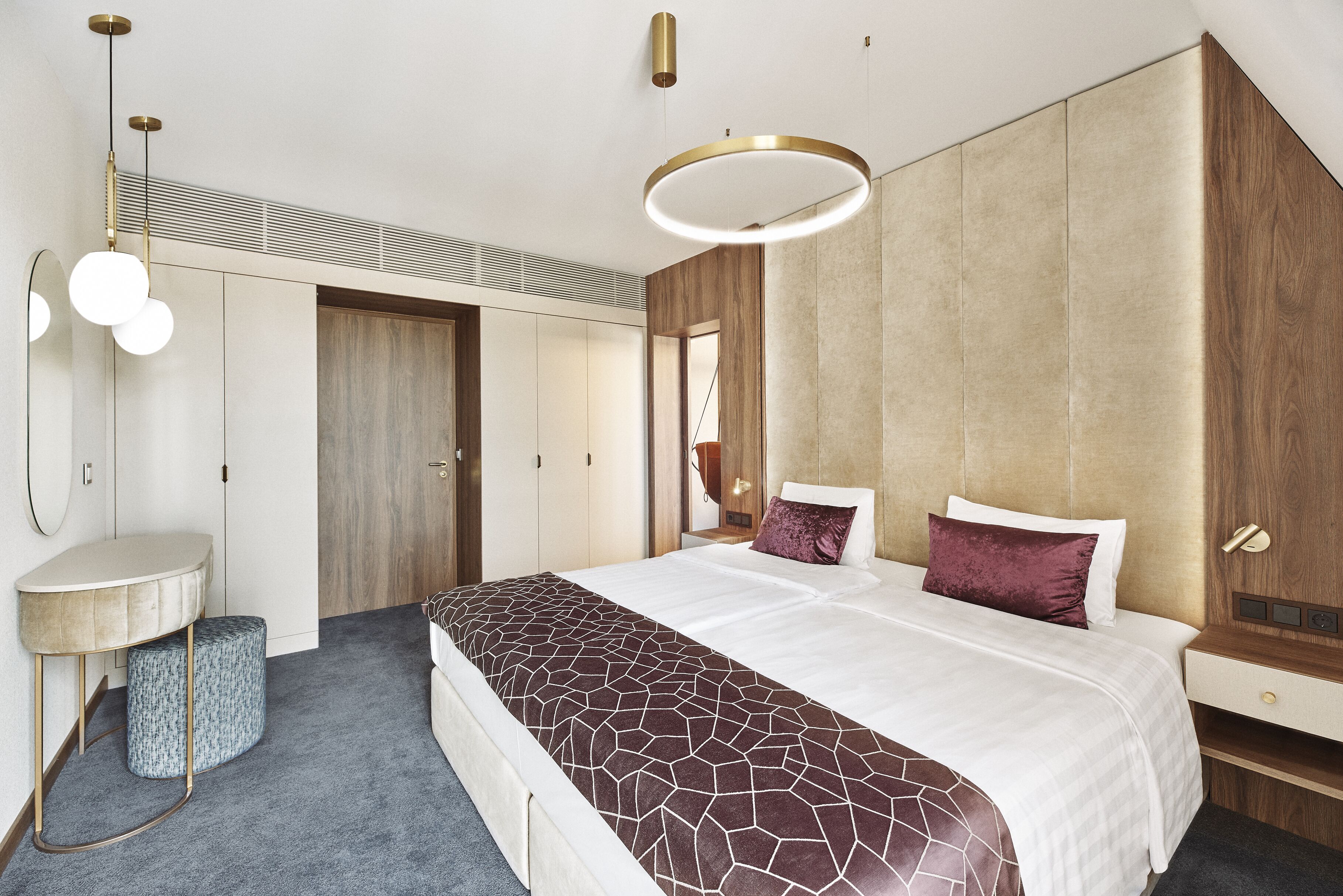 A modern bedroom with a large bed, a bedside table, a mirror, and a built-in wardrobe.