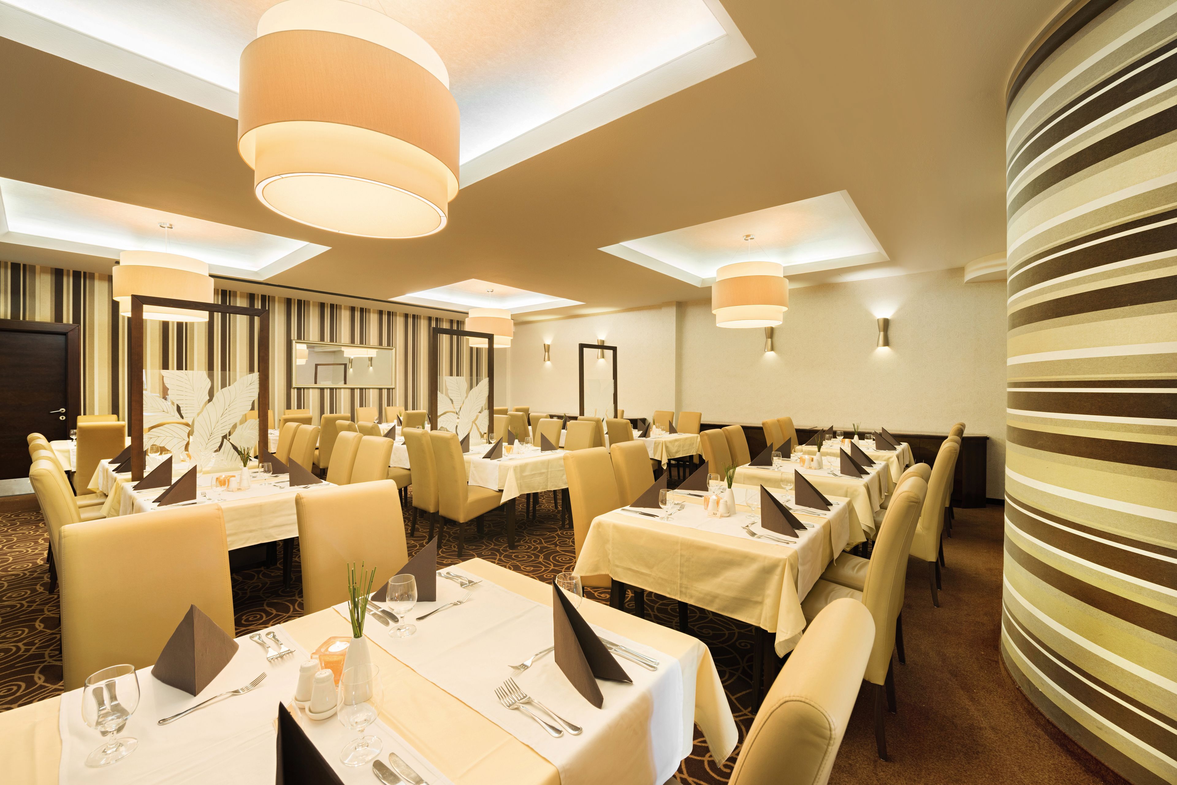 A hotel dining area with multiple tables, chairs, and ceiling lights.