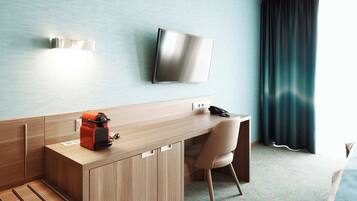 A hotel room with a wooden desk, a chair, a flat-screen TV mounted on the wall, and a window with curtains.
