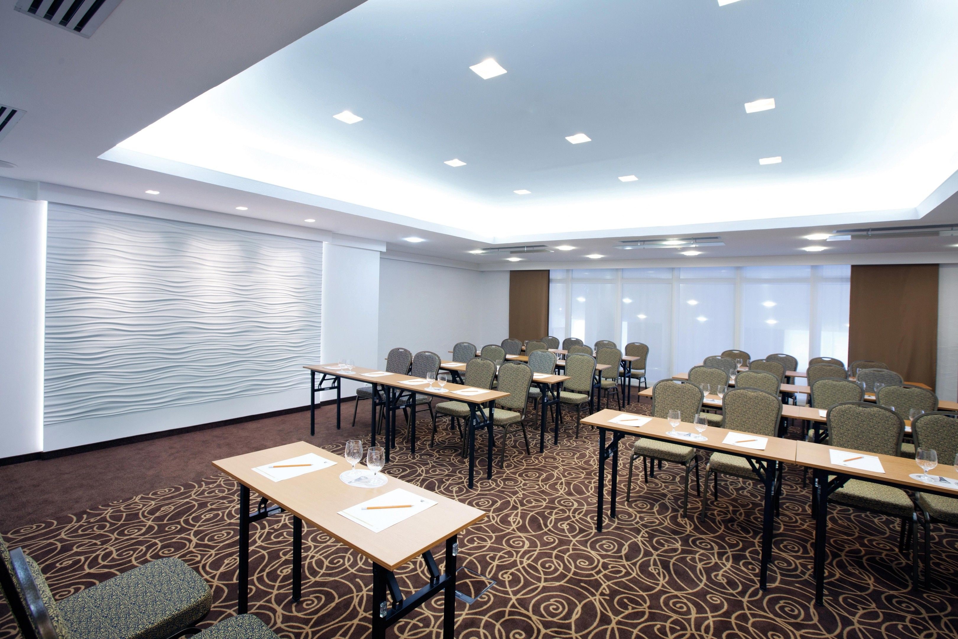 A conference room with multiple tables and chairs, a patterned carpet, and a modern ceiling design.