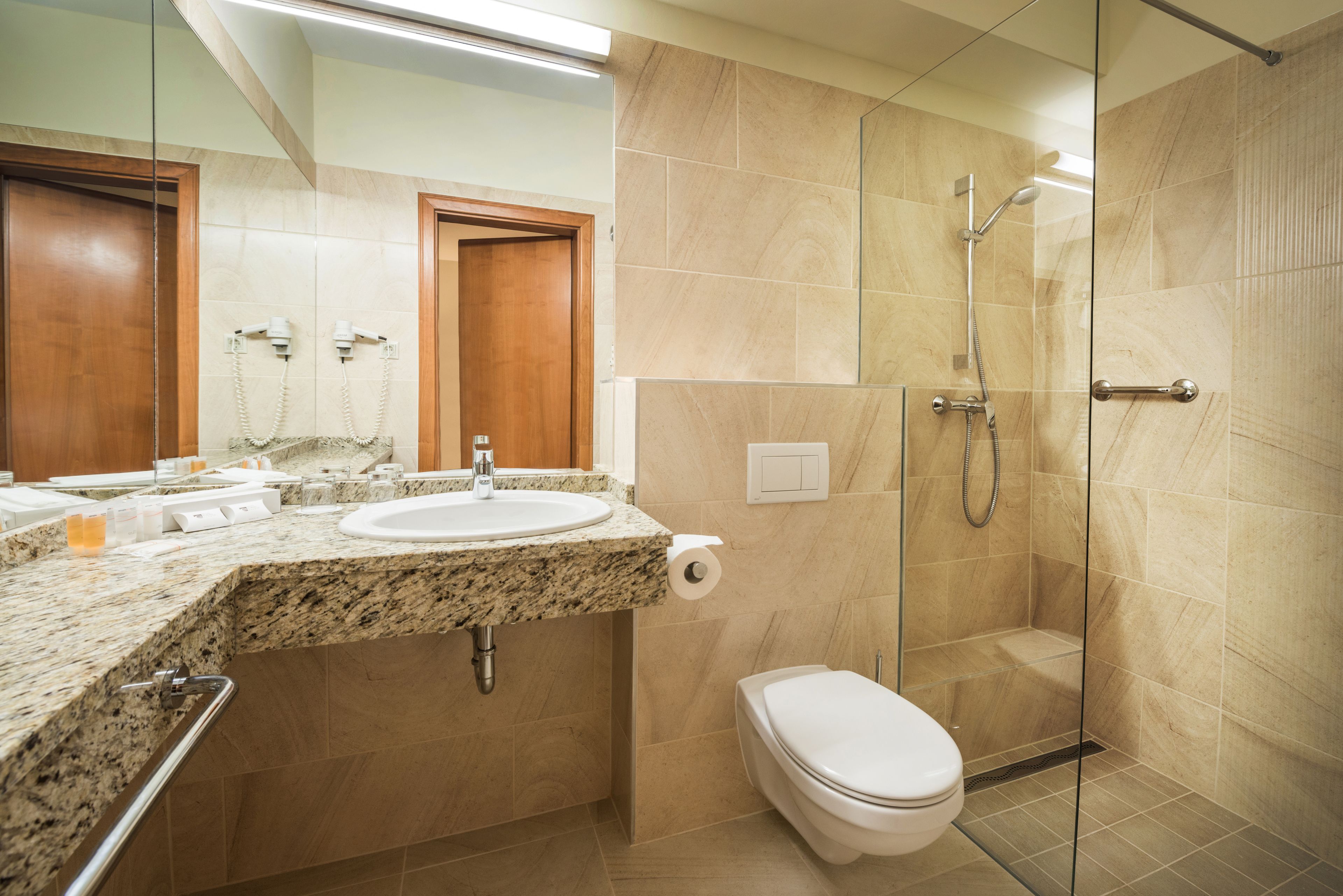 A modern bathroom with a granite countertop sink, a toilet, and a glass-enclosed shower.