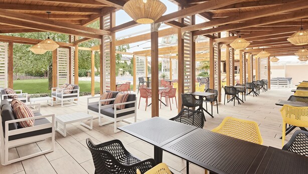 An outdoor patio area with wooden beams, tables, chairs, and hanging lights. - Hotel Európa Fit (Hévíz)