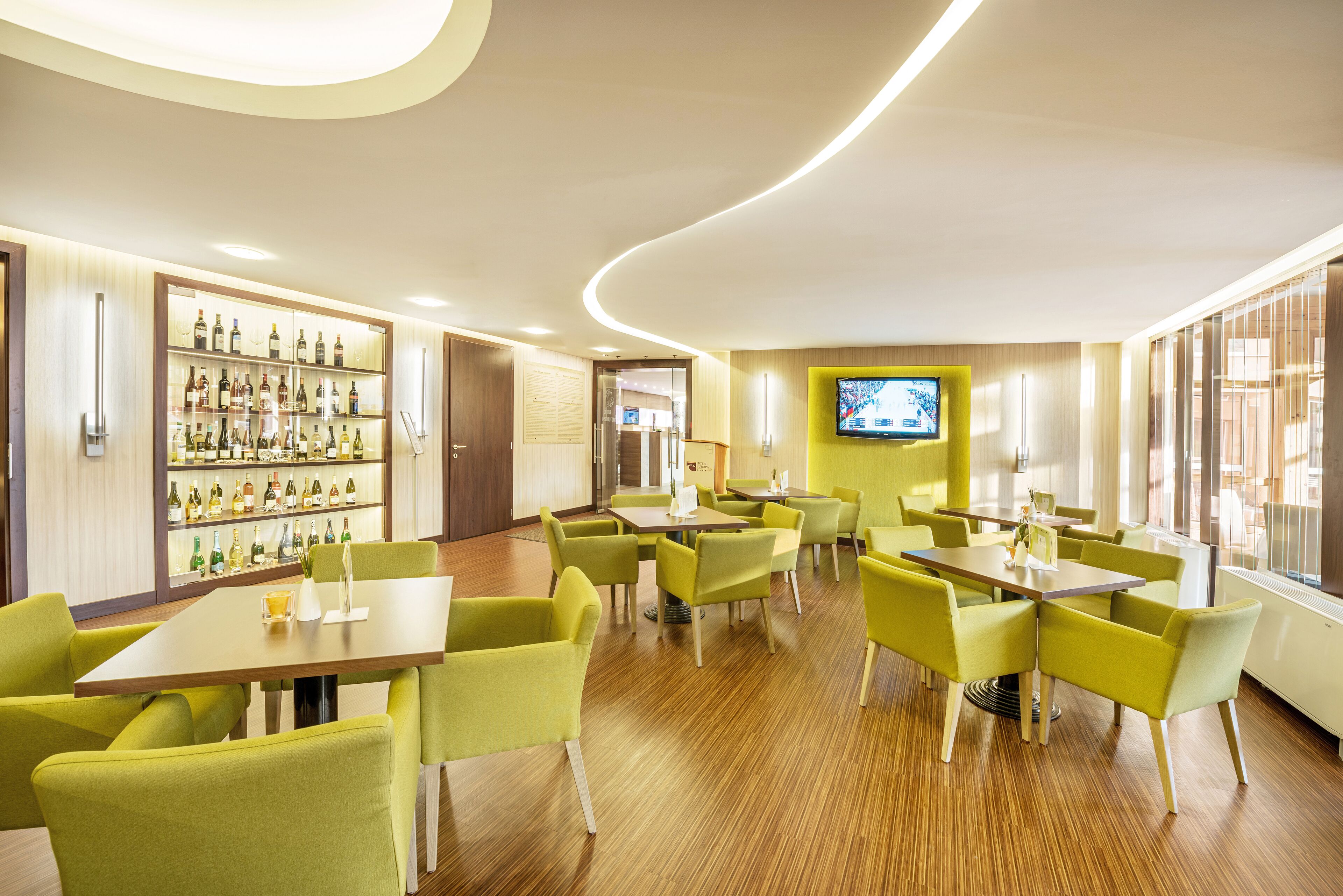 A modern hotel lobby with a bar area, multiple seating arrangements, and a television screen.