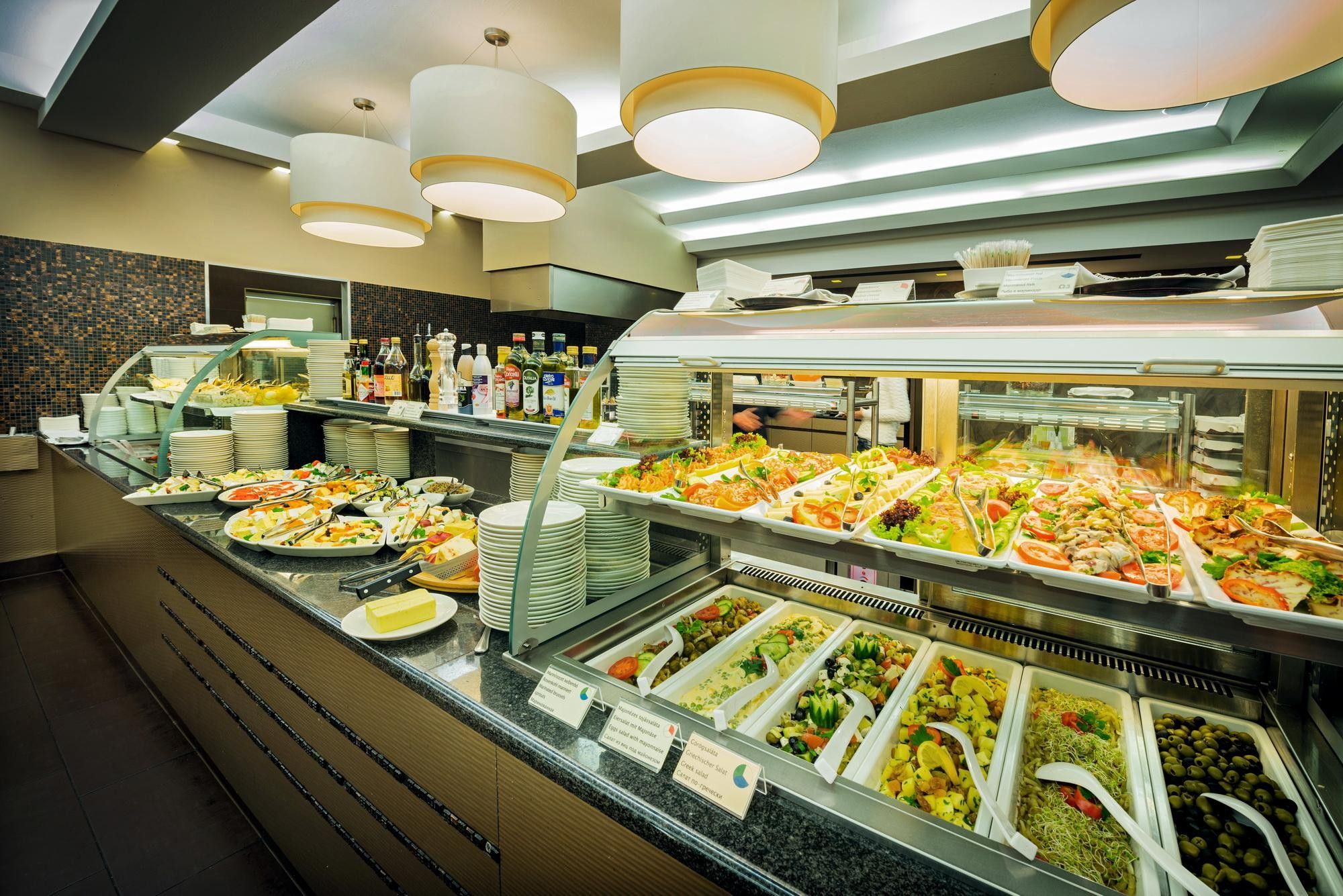 Un buffet proposant une variété de plats, notamment des salades, des viandes et des fromages, avec un décor intérieur moderne et un éclairage suspendu.