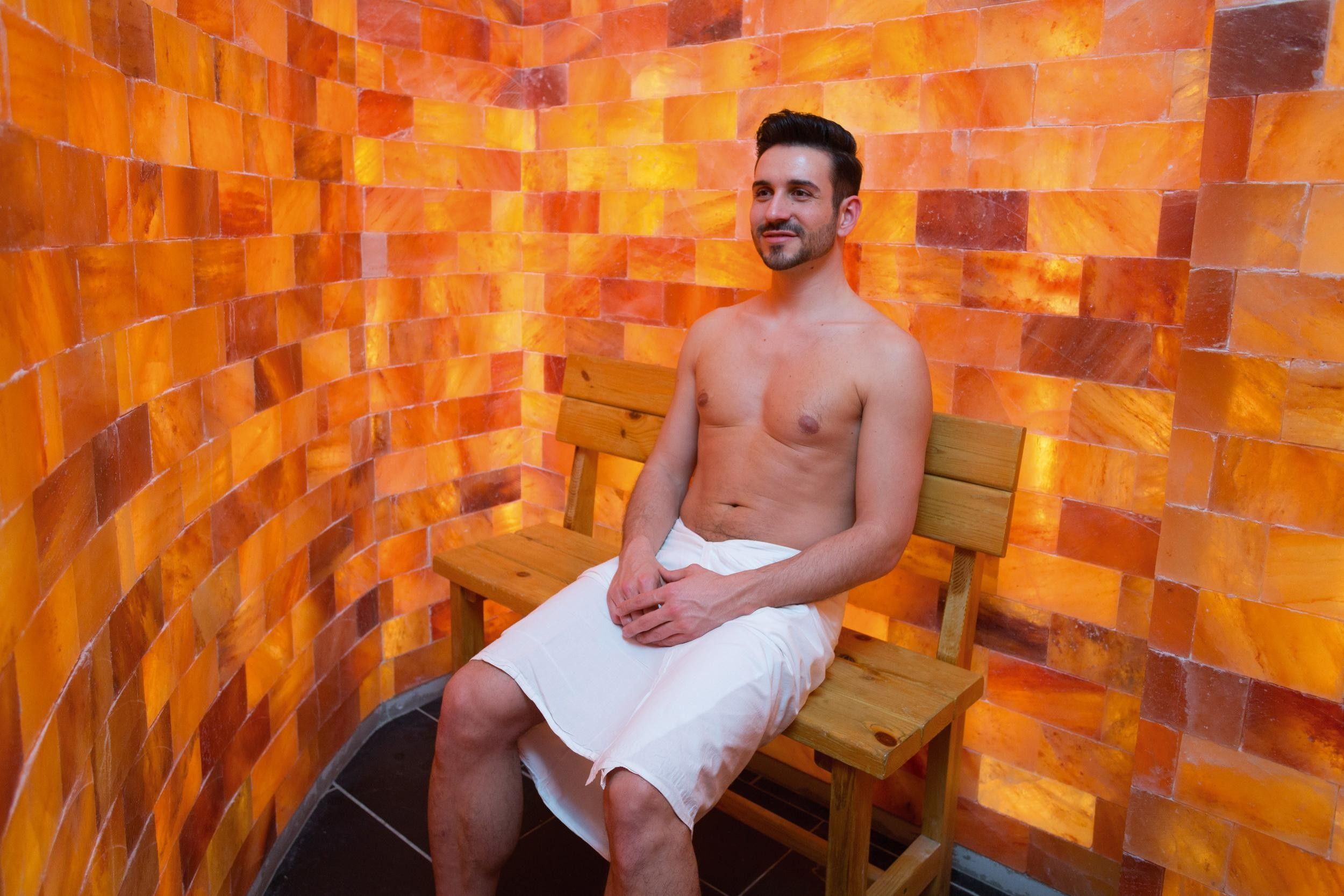 A person seated on a wooden bench in a room with a tiled wall.
