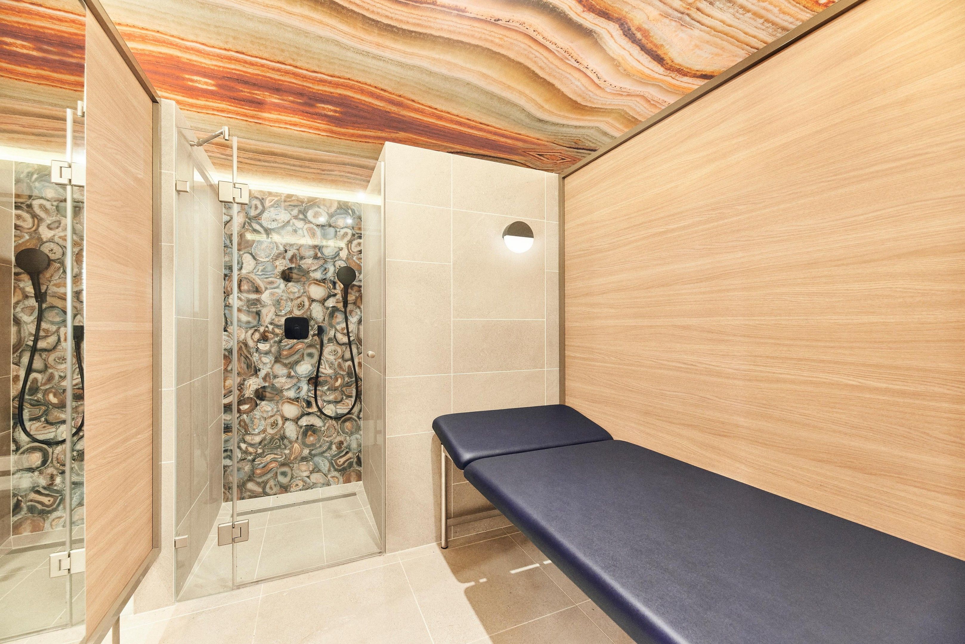 A bathroom with a marble wall, a shower area, and a bench.