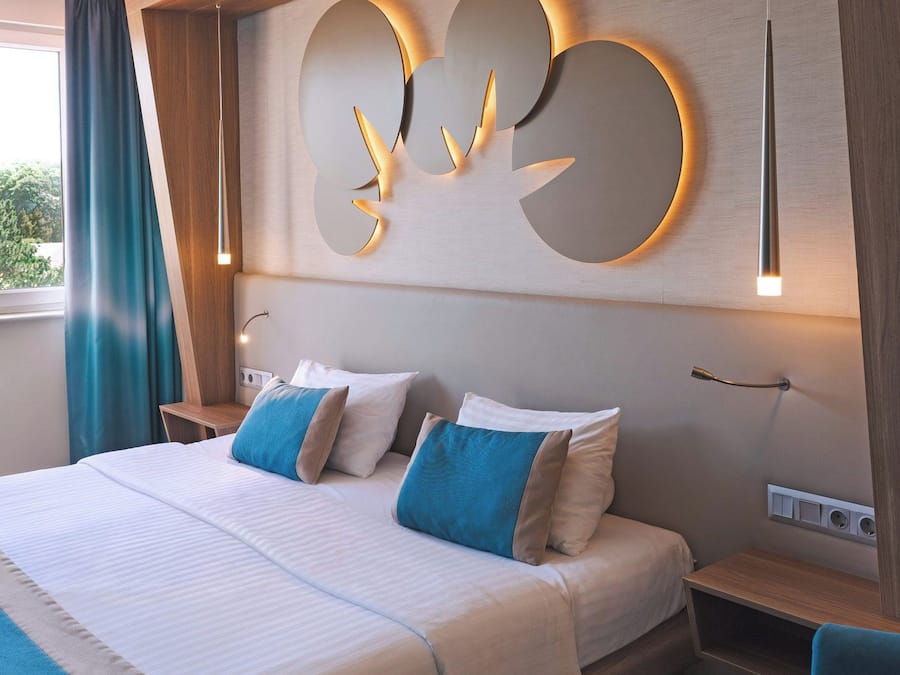 Una habitación de hotel con una cama grande, dos mesitas de noche, una silla y un aplique de pared.