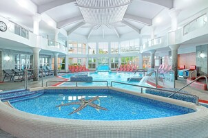Una amplia piscina interior con diseño de estrella de mar, rodeada de sillones de descanso y una estructura de techo moderna.