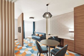 Una habitación de hotel moderna con sofá, mesa de comedor, sillas, televisor y piso con diseño.