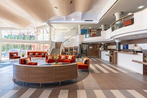 A spacious lobby with a central seating area, a reception desk, and a staircase leading to an upper level. - Hotel Európa Fit (Hévíz)