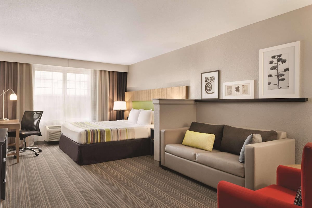 A hotel room with a bed, a sofa, a desk with a chair, and a lamp. There are framed pictures on the wall.