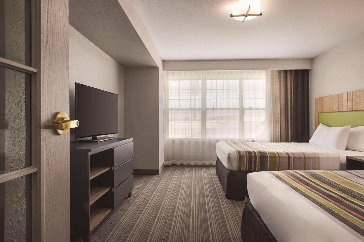 A hotel room with a television on a dresser, a large window with curtains, and a bed with striped bedding.