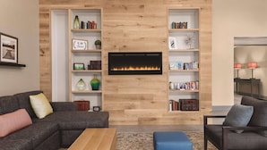 A modern living room with a fireplace, bookshelves, a sofa, and a coffee table. - Country Inn & Suites by Radisson, Green Bay East, WI (Green Bay)