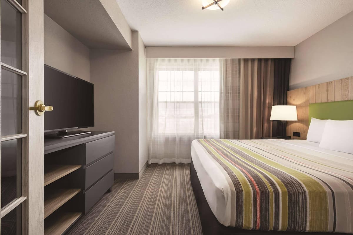 A hotel room with a bed, a TV on a desk, a lamp, and a window with curtains.