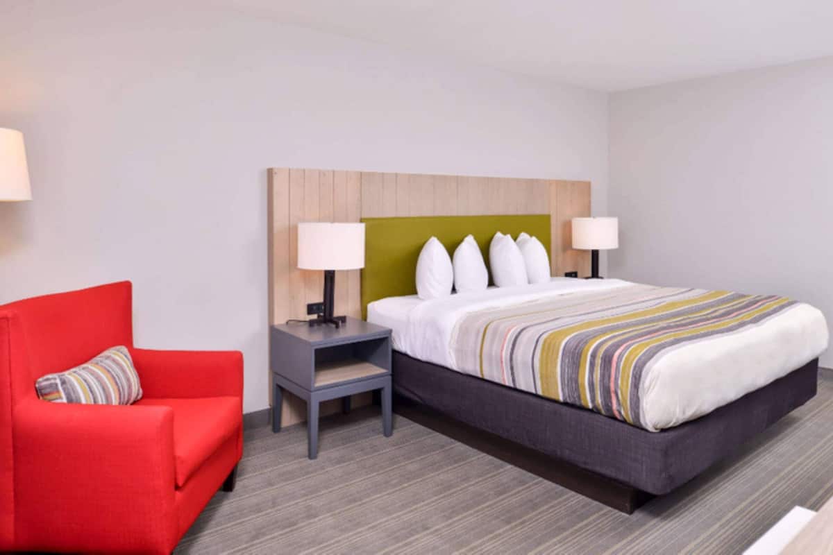 A hotel room with a bed, a red armchair, a nightstand, and two bedside lamps.