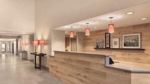 A reception area with a wooden reception desk, pendant lights, framed artwork, and a hallway with a tiled floor. - Country Inn & Suites by Radisson, Green Bay East, WI (Green Bay)