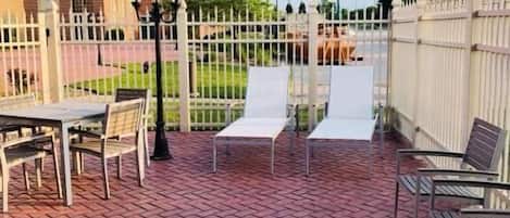 A patio area with brick flooring, white metal chairs, and a table.