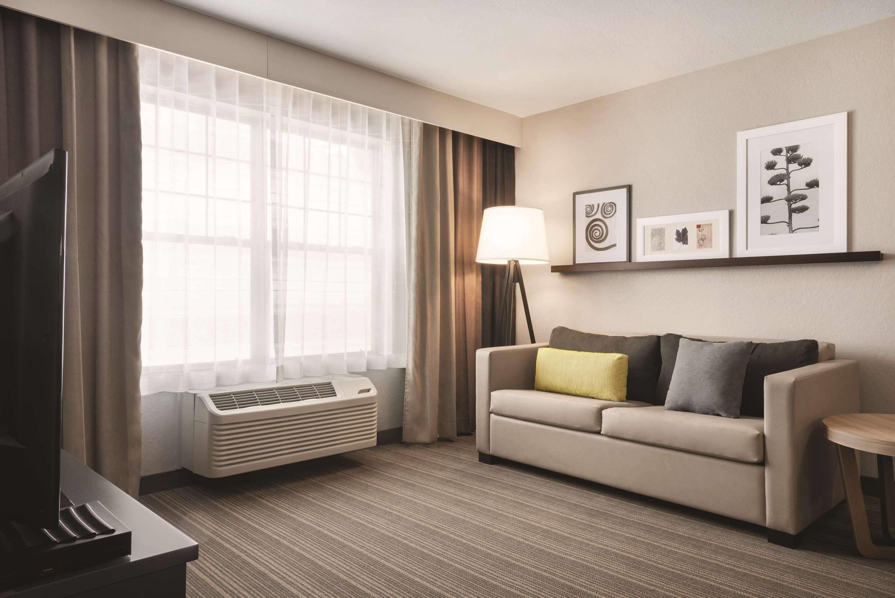 A hotel room with a sofa, a TV, a lamp, and a window with curtains.