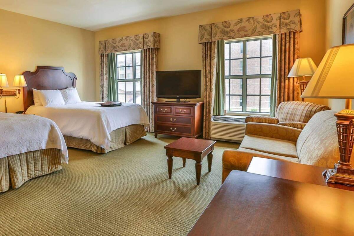 A hotel room with two beds, a television, a sofa, a small table, and a lamp.