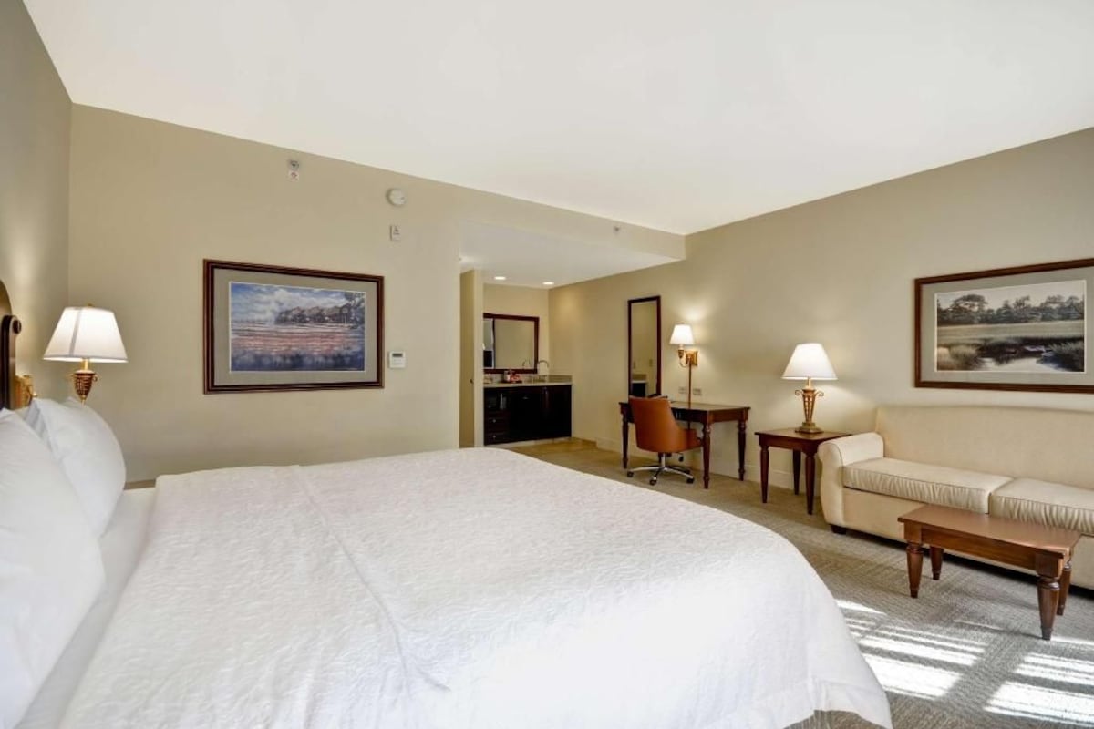 A hotel room with a large bed, a desk, a chair, a sofa, and two lamps.