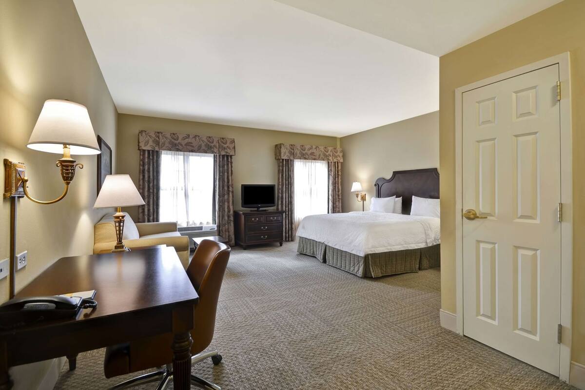 A hotel room with a bed, a desk with a chair, a television, and a door.