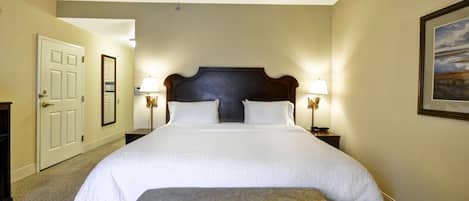 Une chambre d’hôtel avec un grand lit, deux lampes de chevet, une porte, un miroir et un tableau encadré au mur.