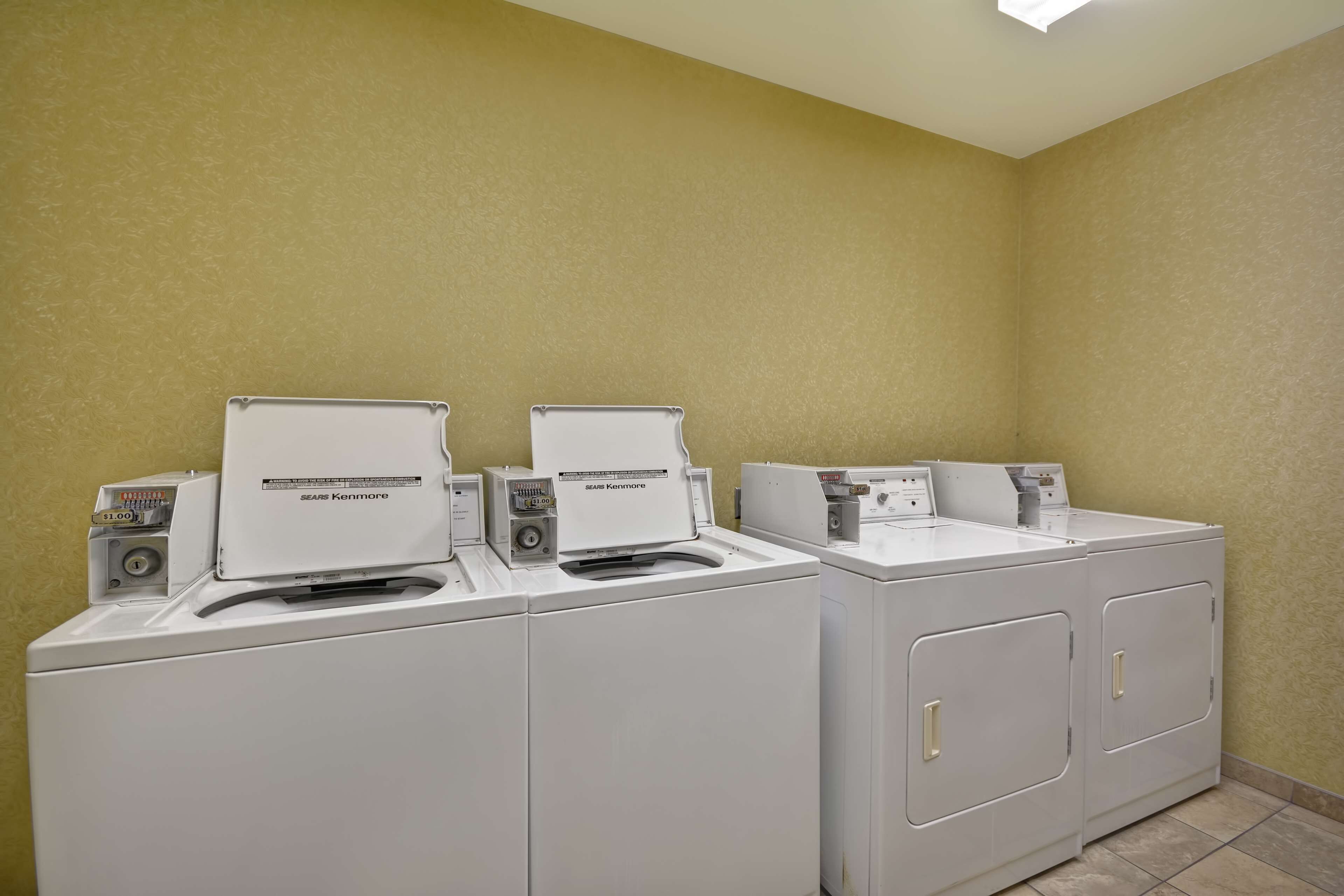 Eine Reihe von weißen Kenmore Frontlader Waschmaschinen und Trocknern in einem Waschraum mit beige gestrichenen Wänden und Fliesenboden.