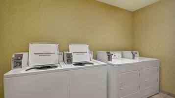 Eine Reihe von weißen Kenmore Frontlader Waschmaschinen und Trocknern in einem Waschraum mit beige gestrichenen Wänden und Fliesenboden.