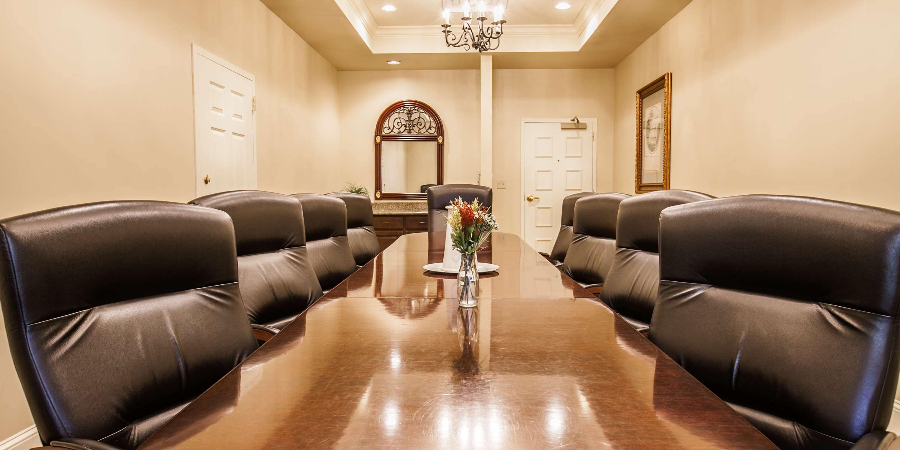 A conference room with a long table and leather chairs, a chandelier, and a mirror on the wall.