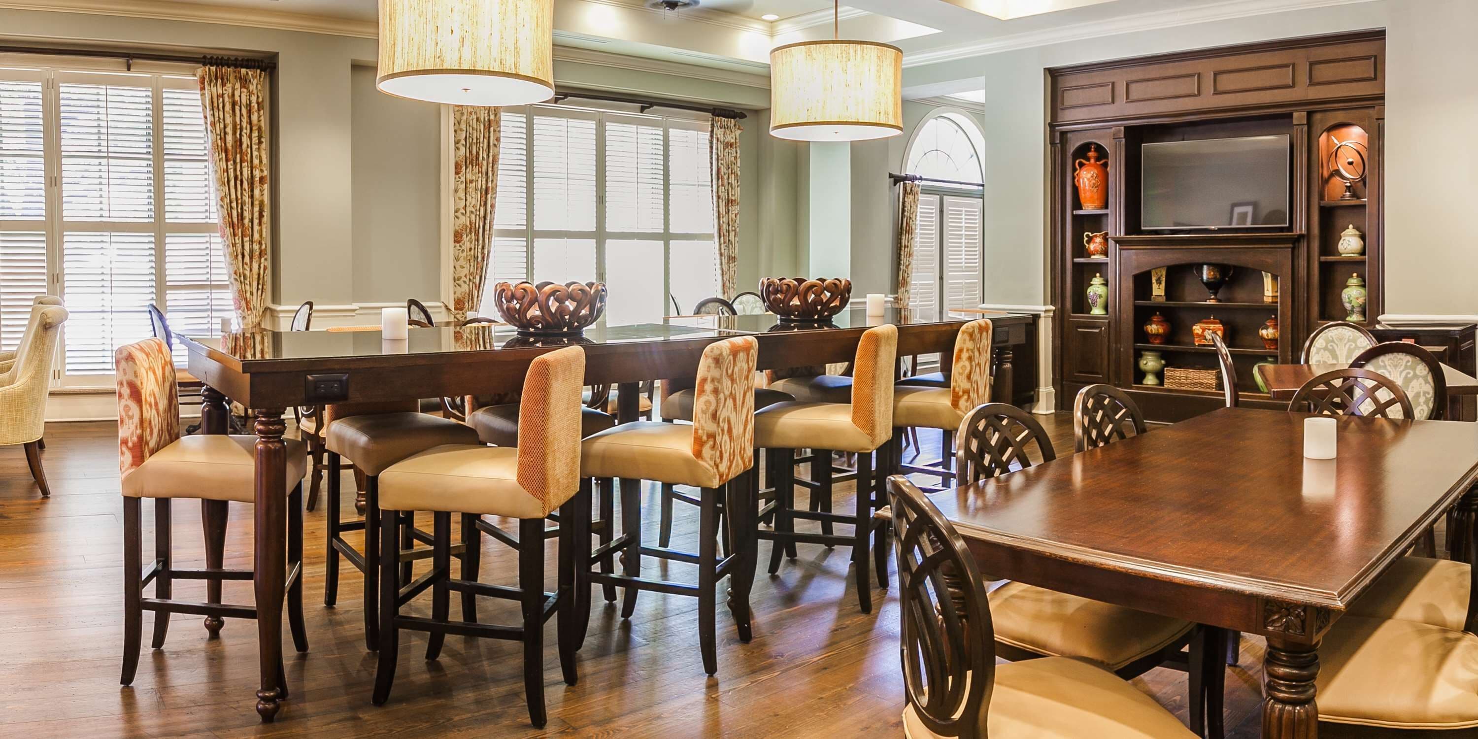 A dining area with a wooden table and bar stools, a chandelier, and a decorative cabinet with pottery.