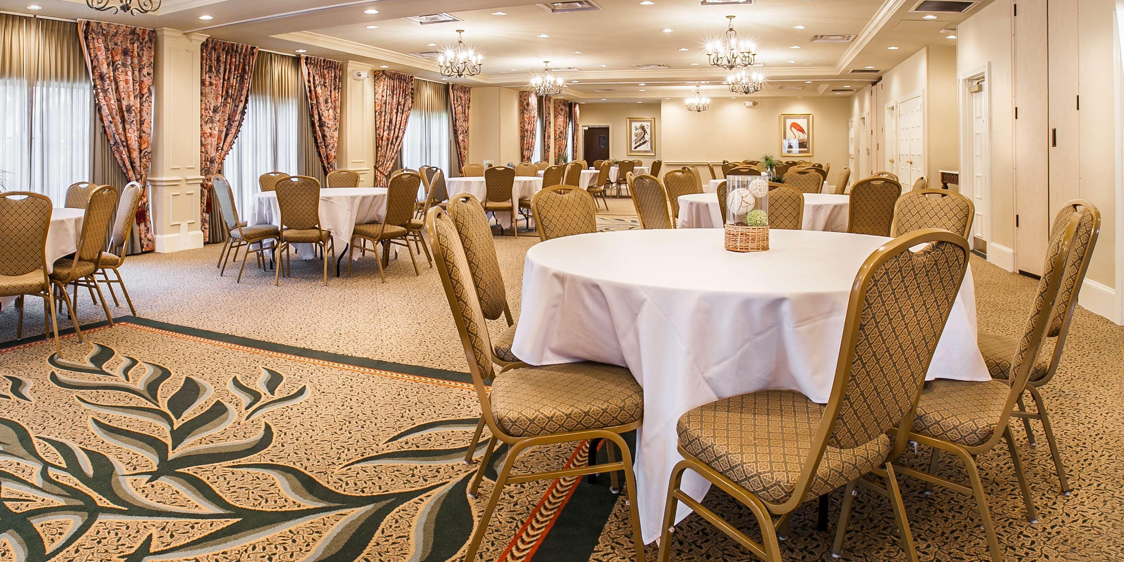 A hotel conference room with round tables, chairs, and a carpet with a leaf pattern.