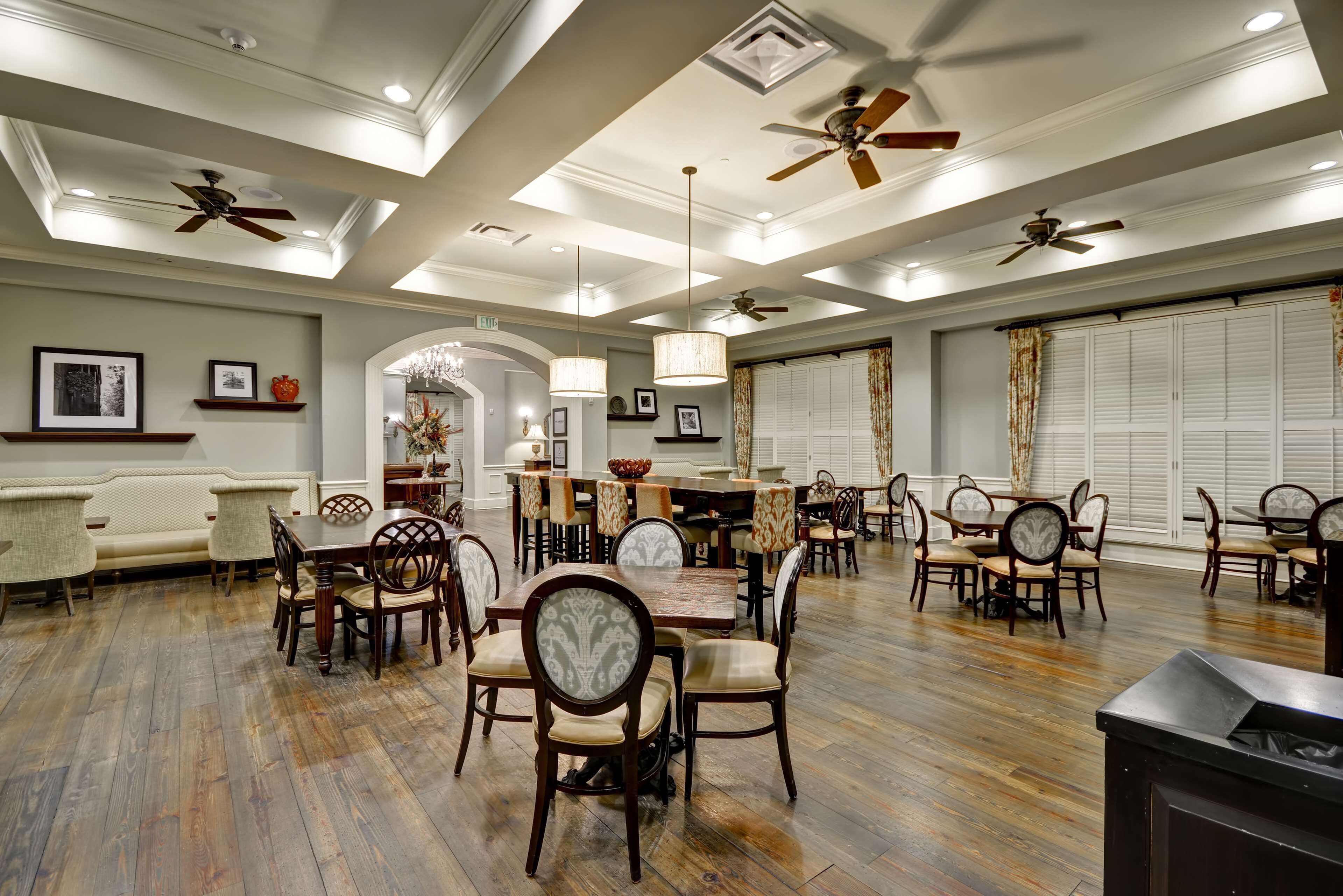 A spacious dining area with wooden flooring, multiple dining tables, and chairs.