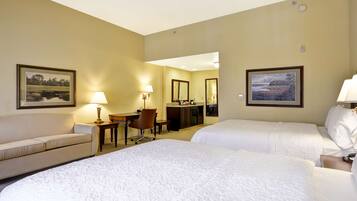 Een hotelkamer met twee bedden, een bureau, een stoel, een lamp en ingelijste foto’s aan de muur.