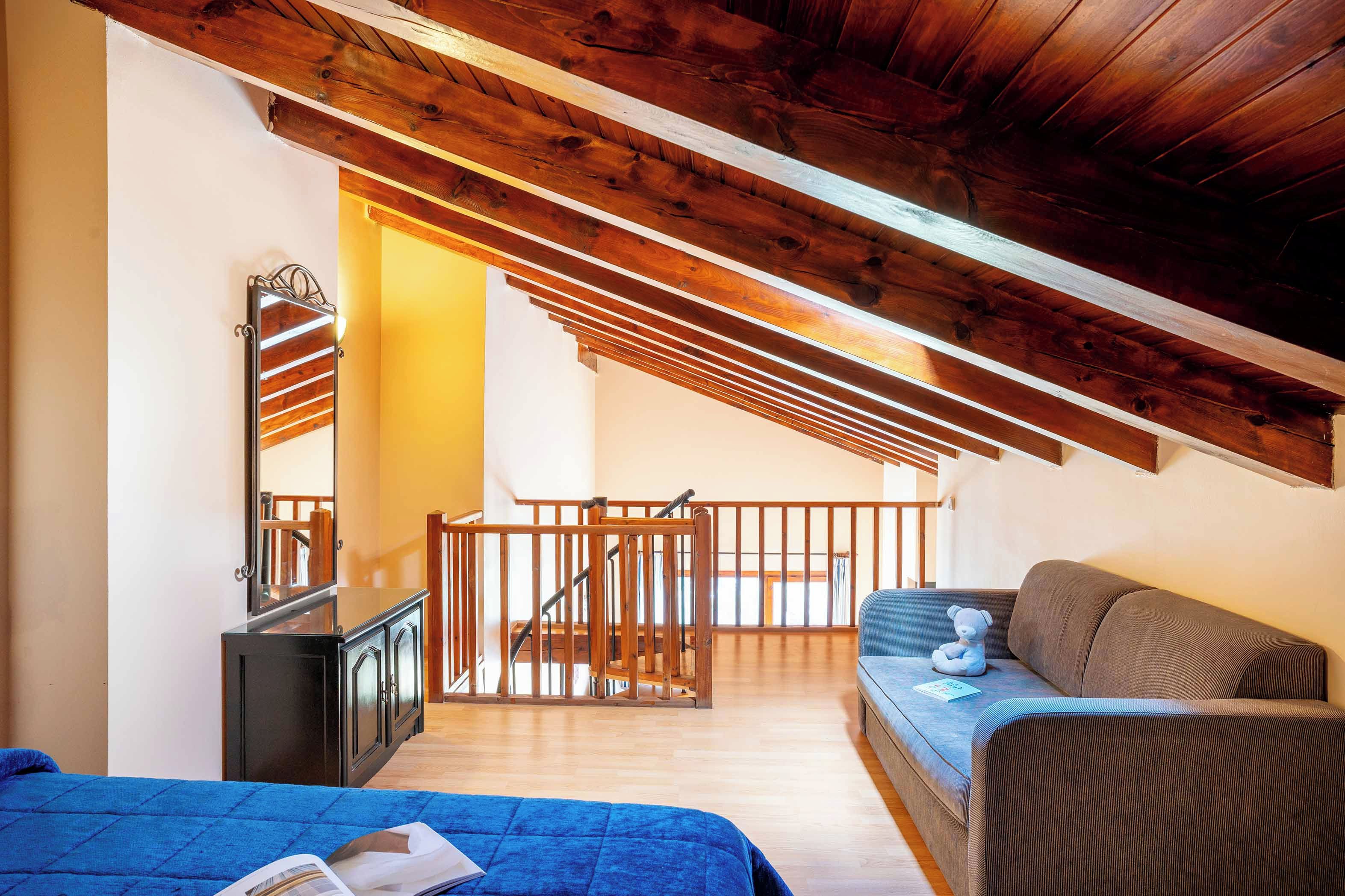 Un dormitorio con techo inclinado, vigas de madera, una cama, un sofá y un espejo.