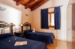 A bedroom with two beds, a nightstand, a lamp, a mirror, and a window with curtains.