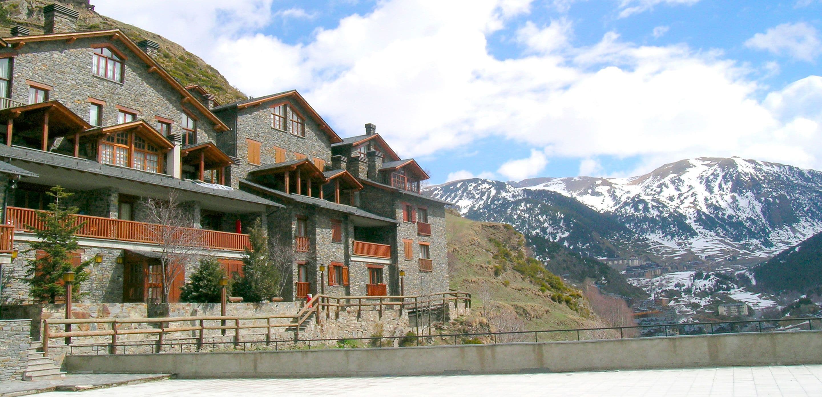 A multi-story stone building with balconies and wooden railings, set against a backdrop of snow-capped mountains.