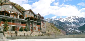 A multi-story stone building with balconies and wooden railings, set against a backdrop of snow-capped mountains. - Apartamentos Ona Dorada el Tarter (Ransol)