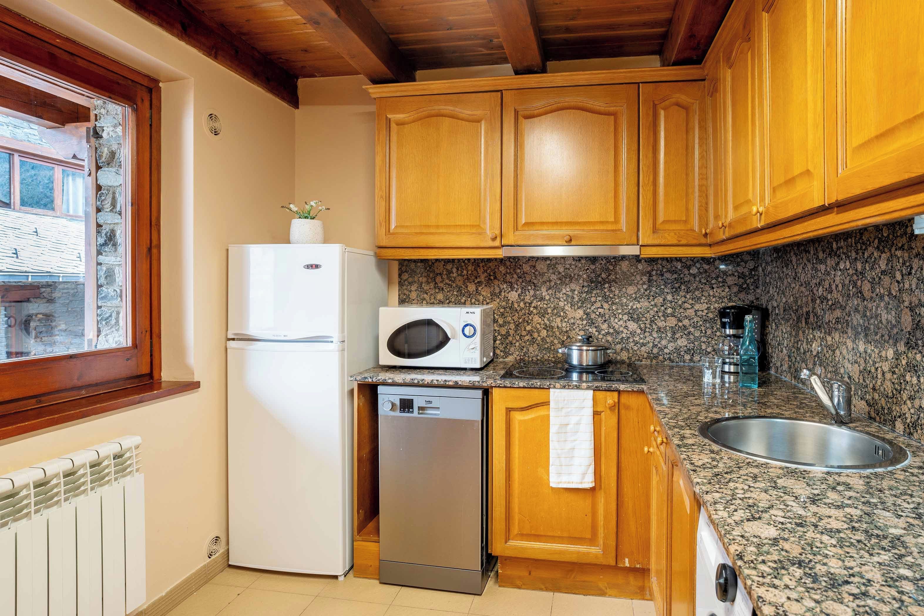 A compact kitchen with wooden cabinets, a built-in microwave, a dishwasher, and a granite countertop.