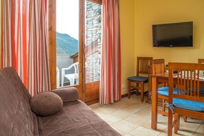 A room with a brown sofa, wooden chairs, a TV on the wall, and a view of mountains through the window. - Apartamentos Ona Dorada el Tarter (Ransol)