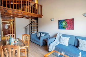 A spacious living area with a wooden staircase, a blue sofa set, a dining table with chairs, and a colorful abstract painting on the wall. - Apartamentos Ona Dorada el Tarter (Ransol)