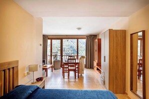 A hotel room with a bed, a desk, a chair, a table, a lamp, a wardrobe, and a view of the outdoors. - Apartamentos Ona Dorada el Tarter (Ransol)