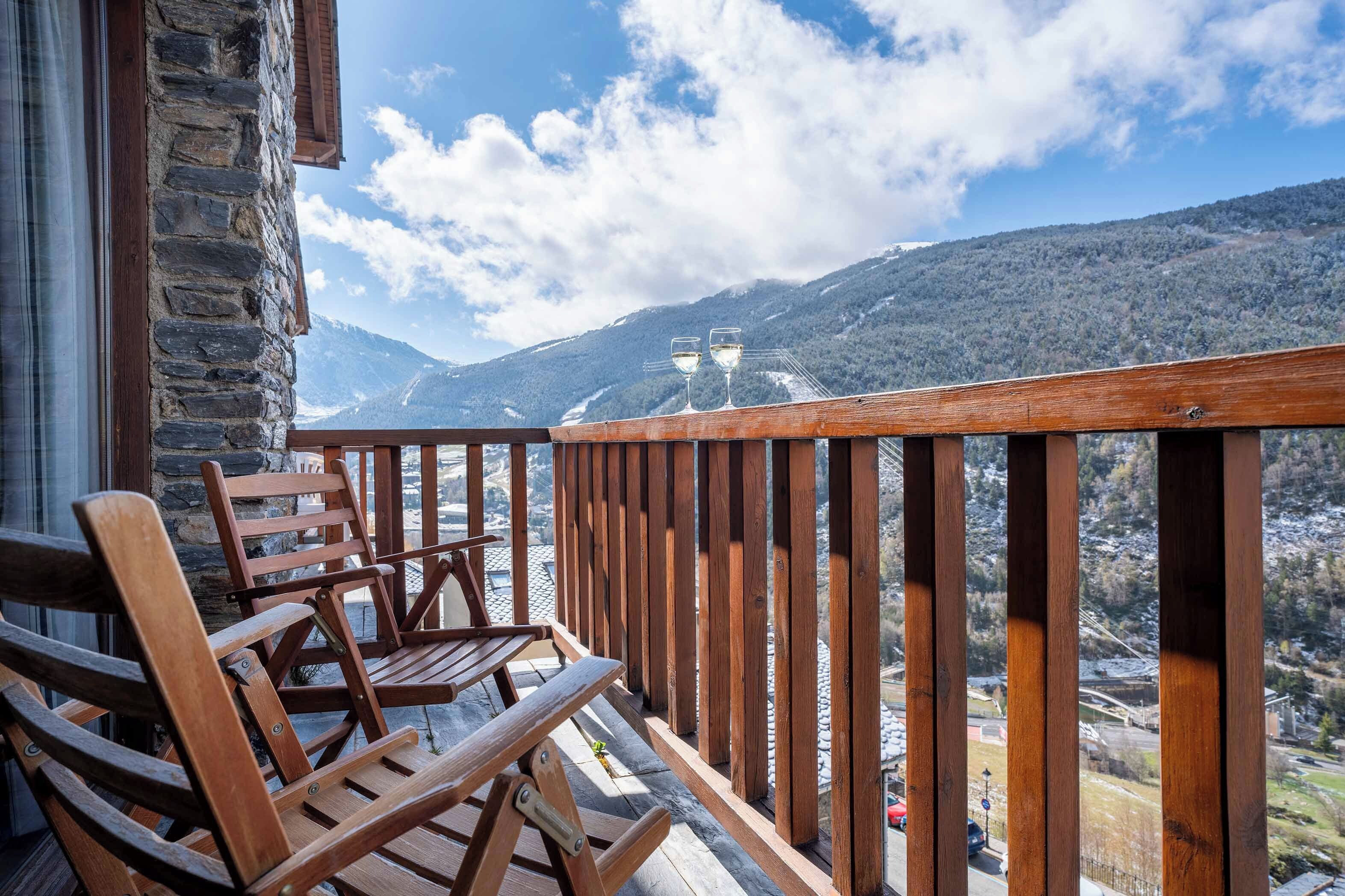 A wooden deck with a stone wall, two wooden chairs, and a view of a mountainous landscape.