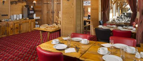 A dining area with wooden tables, red chairs, and a buffet counter with food items.
