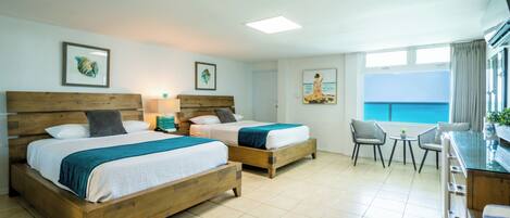 A hotel room with two wooden beds, a small dining table, and a view of the sea.