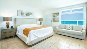 A modern hotel room with a large bed, a sofa, a desk, and a window with a view of the sea. - Villa Cofresi Hotel (Rincon)