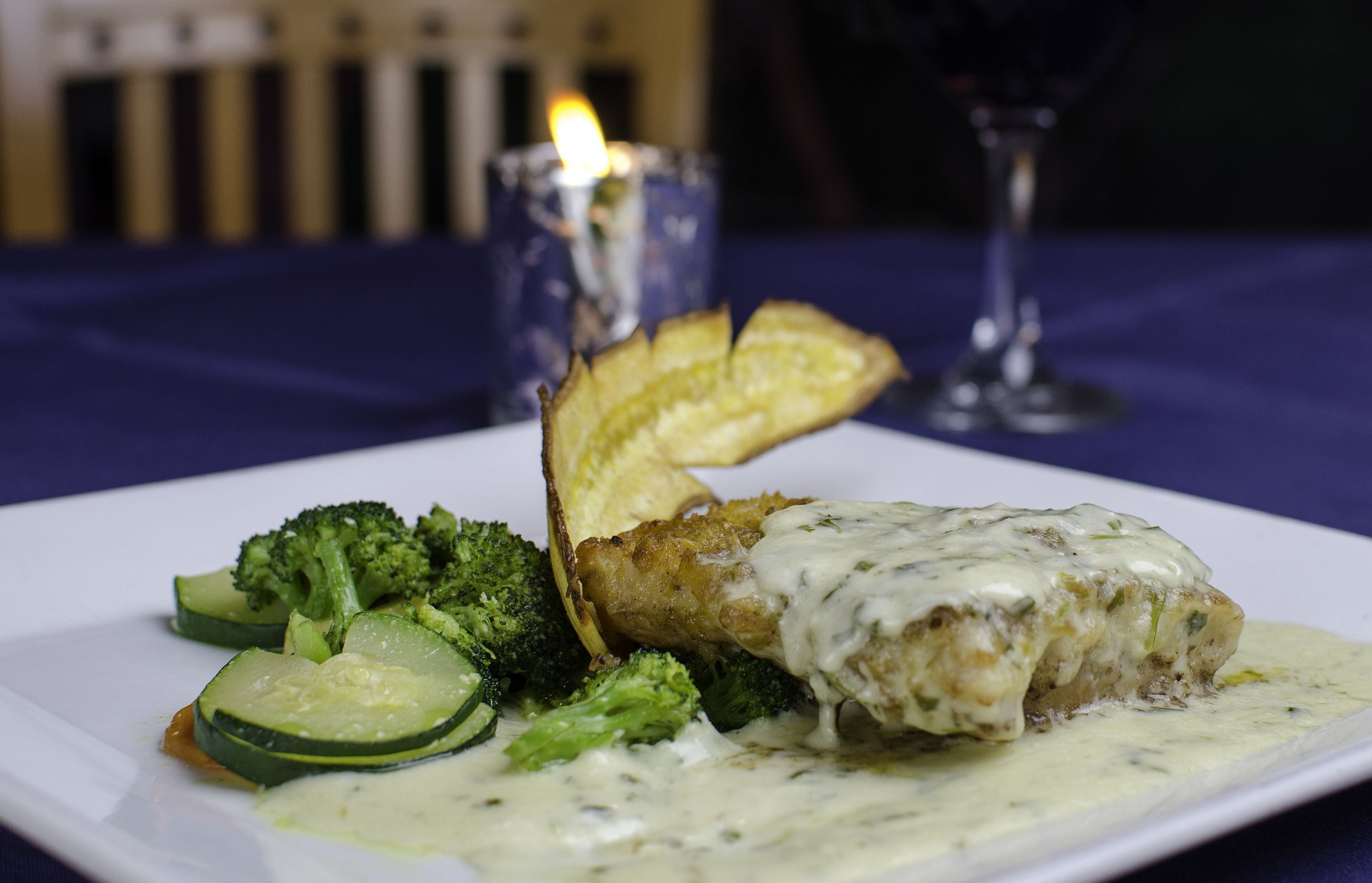 Een bord eten met een romige saus, broccoli en plakjes aardappel.