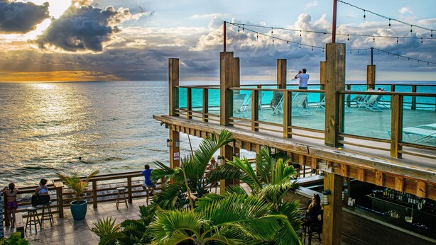 A wooden deck with a bar area and outdoor seating overlooking the ocean. - Villa Cofresi Hotel (Rincon)